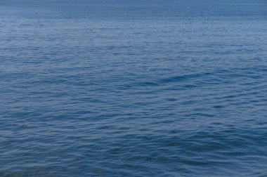 Gün ortası güneşinin altında, sakin denizlerde hafif dalgalar dans ediyor, sahil şeridinde huzur ve sükuneti çağrıştırıyor..