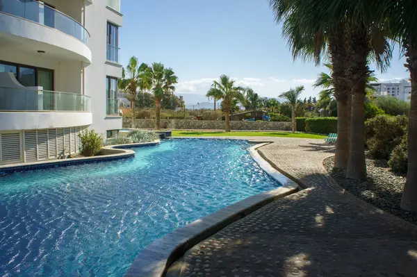 Güneşin altında ışıldayan güzel bir yüzme havuzu, yemyeşil palmiyeler ve sakin çevreler tarafından sarılmıştır..