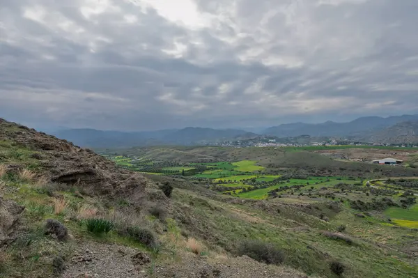 Geniş bir gökyüzünün altında geniş yeşil alanlar karamsar bulutlarla kaplanmış büyüleyici bir manzara yaratıyor..