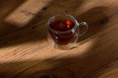 Yumuşak bir fincandan buhar yükselir, dokulu ahşap bir yüzey üzerinde zengin, aromatik çayla dolu..