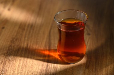 Sıcak, güzel kokulu çayla dolu bir bardak, yumuşak öğleden sonra ışığıyla aydınlatılmış, ahşap bir masada oturur..