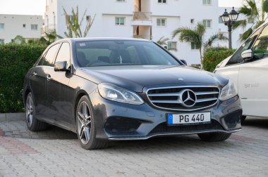 Gaziveren Kıbrıs Rum Kesimi - 30.01.2025 Şık siyah bir sedan palmiye ağaçları ve çağdaş mimariyle çevrili sakin bir otoparkta dinleniyor.