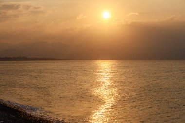 Sersemletici bir günbatımı sakin sularda altın renkler bırakır, bulutlar uzak dağların üzerinden geçerken usulca yansıtır..