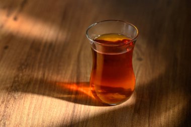 Nefis bir fincan kehribar çayı, parlak ahşap bir yüzeyde oturur. Sıcak öğleden sonra güneşi yumuşak gölgeler bırakır..