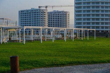 Geniş bir açık hava yemek alanı sıcak öğleden sonra ışığı altında parıldıyor. Parlak binalarla çerçevelenmiş..