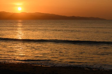 Altın güneş ışığı, gündüzün huzurlu bir sahil şeridi boyunca geceye dönüşmesi gibi yumuşak dalgaları yansıtır..