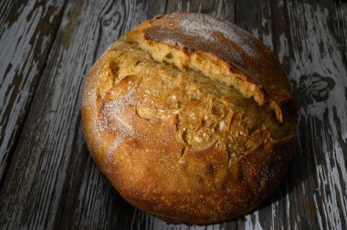 Yuvarlak bir somun eskimiş ahşap bir masanın üzerinde oturur, kabuklu, altın yüzeyi ile davet eder.