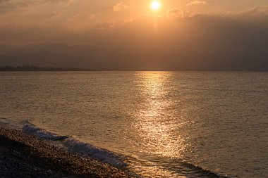 Parlayan günbatımı, sakin denize sıcak bir ışık salıyor. Plajda yumuşak dalgalarla sakin bir atmosfer yaratıyor..