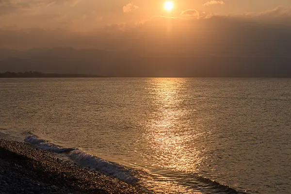 Parlayan günbatımı, sakin denize sıcak bir ışık salıyor. Plajda yumuşak dalgalarla sakin bir atmosfer yaratıyor..