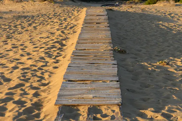 Eski ahşap bir geçit altın kumların üzerine uzanır. Güneş ufukta batarken uzun gölgeler bırakır..