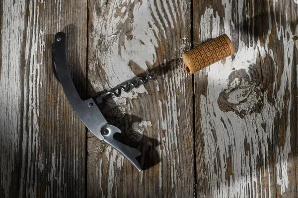 Gümüş bir tirbuşon ve açık kahverengi bir mantar yıpranmış ahşap bir yüzeye oturmuş, kutlamaya ve arkadaşlığa hazır..