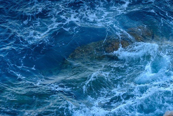 Gentle waves roll over rocky outcrops, shimmering in the sunlight on a peaceful day by the sea.