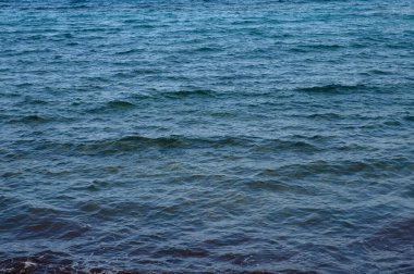 Sakin bir kıyı şeridindeki sakin suların üzerine güneş sıcacık bir parıltı saçarken, yumuşak dalgalar kıyıya vurur..