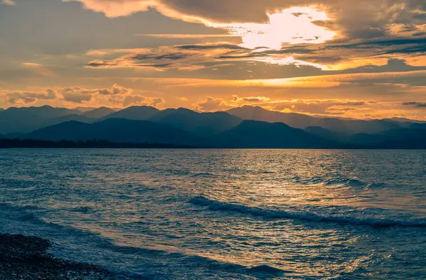 Sıcak renkler gökyüzünü aydınlatırken dalgalar, deniz kenarında huzurlu bir akşamda yavaşça kıyıya vuruyor..