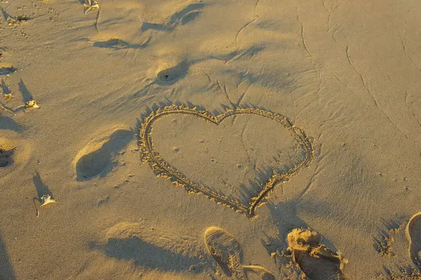 Gün batımının nazik kucaklamasında, kumlarda bir kalp şekli belirir, barışçıl dalgaların yanında aşkı sembolize eder.