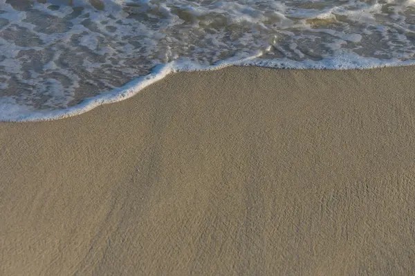 Güneş batarken yumuşak dalgalar sıcak kumu kucaklıyor ve huzurlu bir sahil atmosferi yaratıyor..