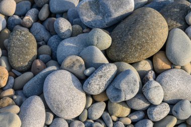 Renkli, pürüzsüz taşlar bir arada uzanmış, sakin bir nehrin yanında doğal güzellikler sergiliyor..