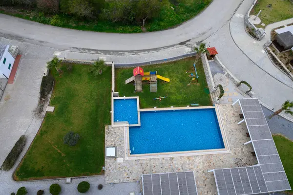 Canlı oyun alanı ekipmanları açık mavi bir havuzun yanında, yemyeşil bir alanda, parlak bir gökyüzünün altında duruyor..