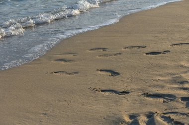 Kumdaki ayak izleri okyanusa doğru gidiyor, sakin bir günbatımı anında dalgalar tarafından nazikçe öpülen..