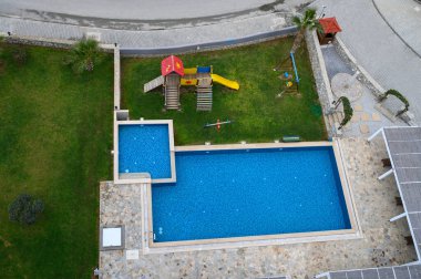 Canlı mavi sular, yemyeşil çimlerle çevrili eğlenceli bir oyun alanı içeren sakin bir havuz alanını geliştirir..