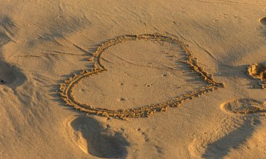 Sıcak kumlu kıyılara kazınmış büyüleyici bir kalp şekli dalgalar usulca kumsalı öperken.