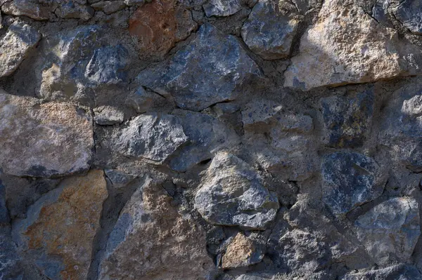 Kaba taşlardan oluşan çeşitli bir düzenleme, yumuşak gün ışığıyla aydınlatılan ve benzersiz dokuları ortaya çıkaran sağlam bir duvar oluşturur..