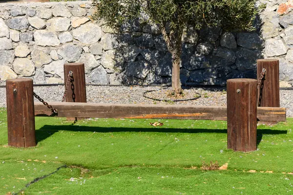 Zincirli ahşap dengeleyici kiriş yeşil çimenlerin üzerinde, taş bir duvar ve yalnız bir ağaç tarafından çerçevelenmiş..