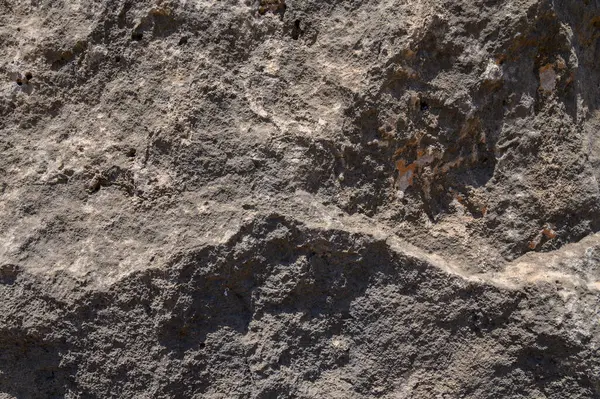 Güneş ışığı engebeli bir kaya yüzeyine gölge düşürür, doğal bir ortamda karmaşık dokuları ve renkleri ortaya çıkarır..