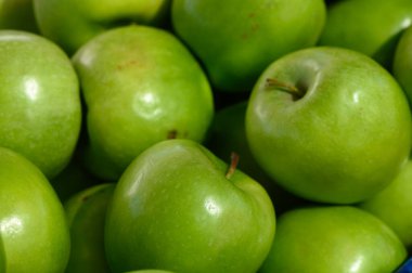 Parlak yeşil elmalar üst üste yığılıp sıcak güneş ışığı altında parlak derilerini sergilerler. Taze dokuları ve tatlı aromaları müşterileri pazarın cömertliğini keşfetmeye davet ediyor..