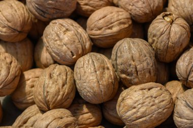 Güneşte kurutulmuş cevizler ahşap bir masaya saçılmış, desenli kabuklarını ve zengin toprak renklerini sergiliyorlar, sıcaklık ve hasat sezonunu anımsatıyorlar..