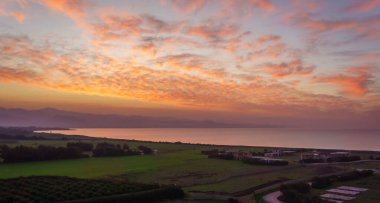 Güneş sakin suların üzerinde batarken ve yemyeşil alanlar yeşerirken canlı renkler gökyüzünü dolduruyor. Huzurlu atmosfer, doğanın güzelliğini yansıtmaya ve takdir etmeye davet eder..