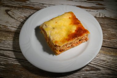 Kahverengi, peynirli bir lazanyanın zevkini çıkarın. Basit bir beyaz tabakta davetkar bir şekilde oturur. Sıcak bir akşam yemeğinde keyiflenmeye hazırdır..