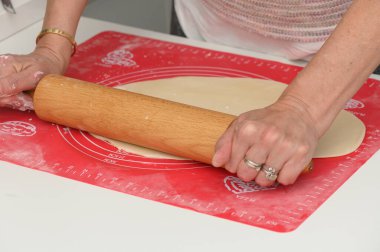 Elleri ustalıkla hamuru sıcak bir mutfakta parlak kırmızı bir paspasın üzerine serer. Mekanı dolduran neşeli bir atmosfer, yemek pişirme ve kahkahalarla dolu güzel bir toplantıyı ima ediyor..