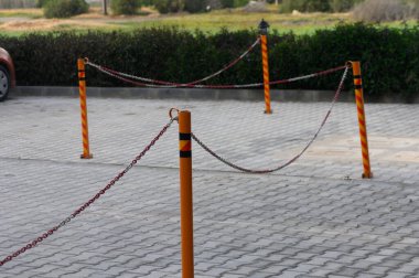 Zincirli parlak renkli direkler, gri asfalt ile çevreleyen yemyeşil zemin arasında uzanan barışçıl bir alanın ana hatlarını çiziyor. Bariyerlerin ötesinde sakin bir kır manzarası görülebilir..