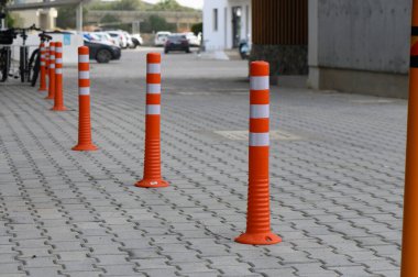 Canlı turuncu kabuklar, güneşli bir günde hareketli bir mahallede modern kentsel tasarım sergilerken yaya güvenliğini teşvik eden kaldırımlı bir yürüyüş yolu boyunca dik dururlar..