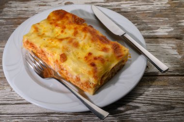 Peynirle köpüren ağız sulandıran bir lazanya dilimi basit beyaz bir tabakta sunulur. Çatal bıçak takımı onun yanında duruyor. Akşam karanlığında bu konforlu tabağın tadını çıkarmaları için lokantaları davet ediyor..