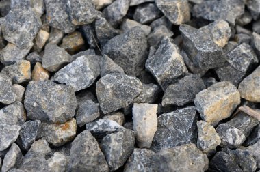 Engebeli gri taşlar bir yüzeye saçılmış, güneş ışığını yansıtıyor ve çeşitli dokular sergiliyor..