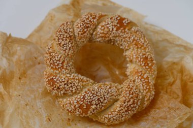 Çok güzel işlenmiş bir susamlı ekmek halkası buruşuk parşömen kağıdının üzerinde duruyor, altın kahverengi kabuğu kabarık iç kısmı vurguluyor. Bu lezzetli ziyafet, zengin aromasıyla baştan çıkarıcı..