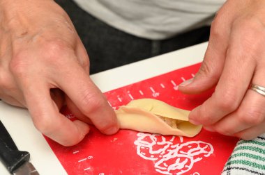 Bir insan lezzetli bir dolguyu kapatmak için kenarlarını dikkatlice katlayarak bir hamur işi ambalajını titizlikle şekillendirirken, yumuşak bir parıltı yağmurlu bir günde davetkar mutfağı doldurur..