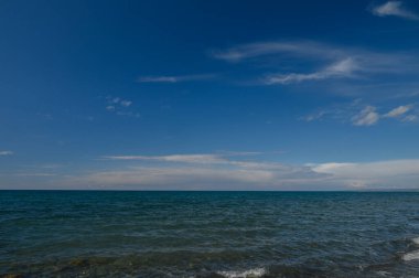 İnce bulutlarla dolu açık mavi bir gökyüzünün altında kıyı şeridine uzanan hafif dalgalar gün doğumunda huzurlu ve sakinleştirici bir atmosfer yaratır..