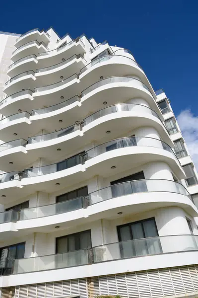 Çarpıcı bir bina, güneşli bir günde çağdaş mimari güzelliği ön plana çıkaran açık mavi gökyüzüne karşı parlak bir cephe ve akan balkonlara sahiptir..