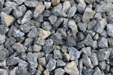 Farklı boyutlarda gri çakıl taşları zemini kaplayarak güzel bir renk ve doku mozaiği oluşturur. Güneş ışığı yüzeyden yansıyarak benzersiz şekilleri ve oluşumları vurgular..