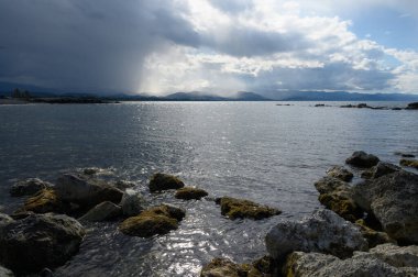 Dalgalar yavaşça kaya çıkıntılarına çarpıyor ufukta karanlık bulutlar belirdikçe sakin bir atmosfer yaratıyor. Alacakaranlık saatlerinde yaklaşan fırtınayı işaret ediyorlar..