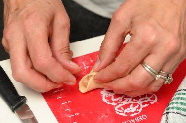 Eller maharetli kırmızı bir tahta üzerinde hamuru ustalıkla katlıyor, güneşli bir öğleden sonra aşçılığın oluşumunun neşesini yansıtıyor, arkadaşlarının toplanmasına sıcaklık katıyor..