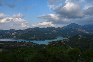 Bereketli yeşil tepeler sakin bir turkuaz gölü besler. Dramatik bulutlar alacakaranlıkta dağların üzerinde sürüklenirken nefes kesici bir doğal manzara yaratır..