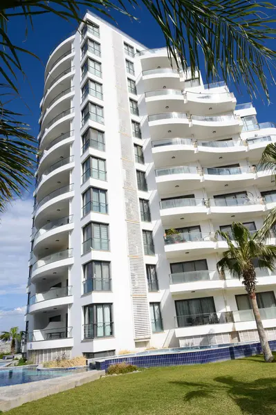 Parıldayan bir havuzun yanında zarif bir apartman dairesi yükselir, yemyeşil palmiyelerle çevrilidir. Parlak güneş ışığı, gökyüzünün çarpıcı zeminine karşı çağdaş tasarımını ön plana çıkarıyor.