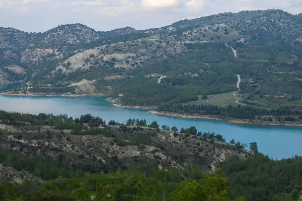 Görkemli dağlar, gökyüzünü yansıtan parlak mavi bir göl oluşturur. Kıyı boyunca uzanan yeşil ağaçlardan oluşan bir duvar halısı, doğanın kucaklamasında sükuneti ve keşfi davet ediyor..