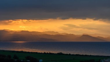 Altın ışık ufukta süzülür, sakin suyu aydınlatır ve dönen dağlara gölge düşürür. Bu resim gibi an, doğanın çarpıcı güzelliğini şafakta yakalar..