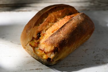 Sıcak, altın zanaatkar ekmek, yumuşak güneş ışığıyla yıkanmış, ahşap bir masada oturur. Kabuğun dokusu taze, ev yapımı doğasını ön plana çıkarıyor, herkesi lezzetinin tadını çıkarmaya davet ediyor..