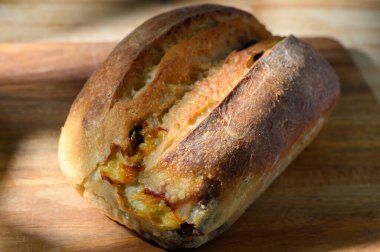 Güzel bir somun zanaatkar ekmeği ahşap bir kesme tahtasının üzerinde duruyor, altın kabuğu yumuşak ışık altında parlıyor. Kahvaltı için ideal ya da akşam yemeği için bir yan olarak, bu ekmek paylaşmayı ve eğlenmeyi davet eder.